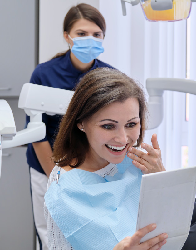 happy middle aged woman with dentist looking mirror teeth sitting dental chair